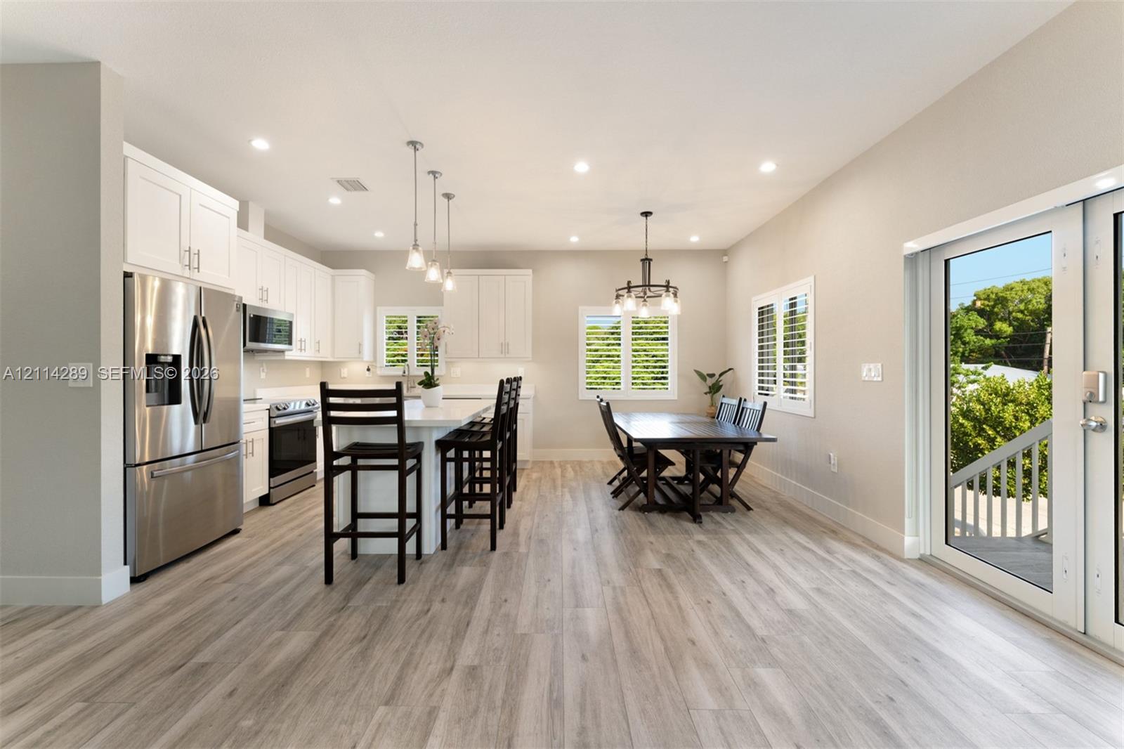 Open-concept kitchen featuring white shaker-style cabinetry, quartz countertops, stainless steel appliances, a center island with pendant lighting, and wood-finish flooring
