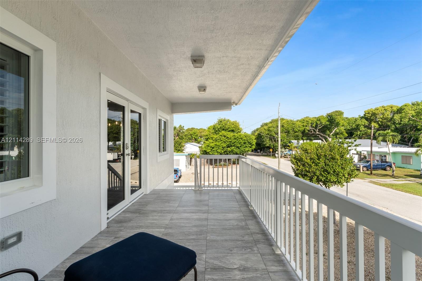 Covered exterior balcony featuring wood-finish tile flooring, white metal railing, recessed lighting, and double-glass door entry