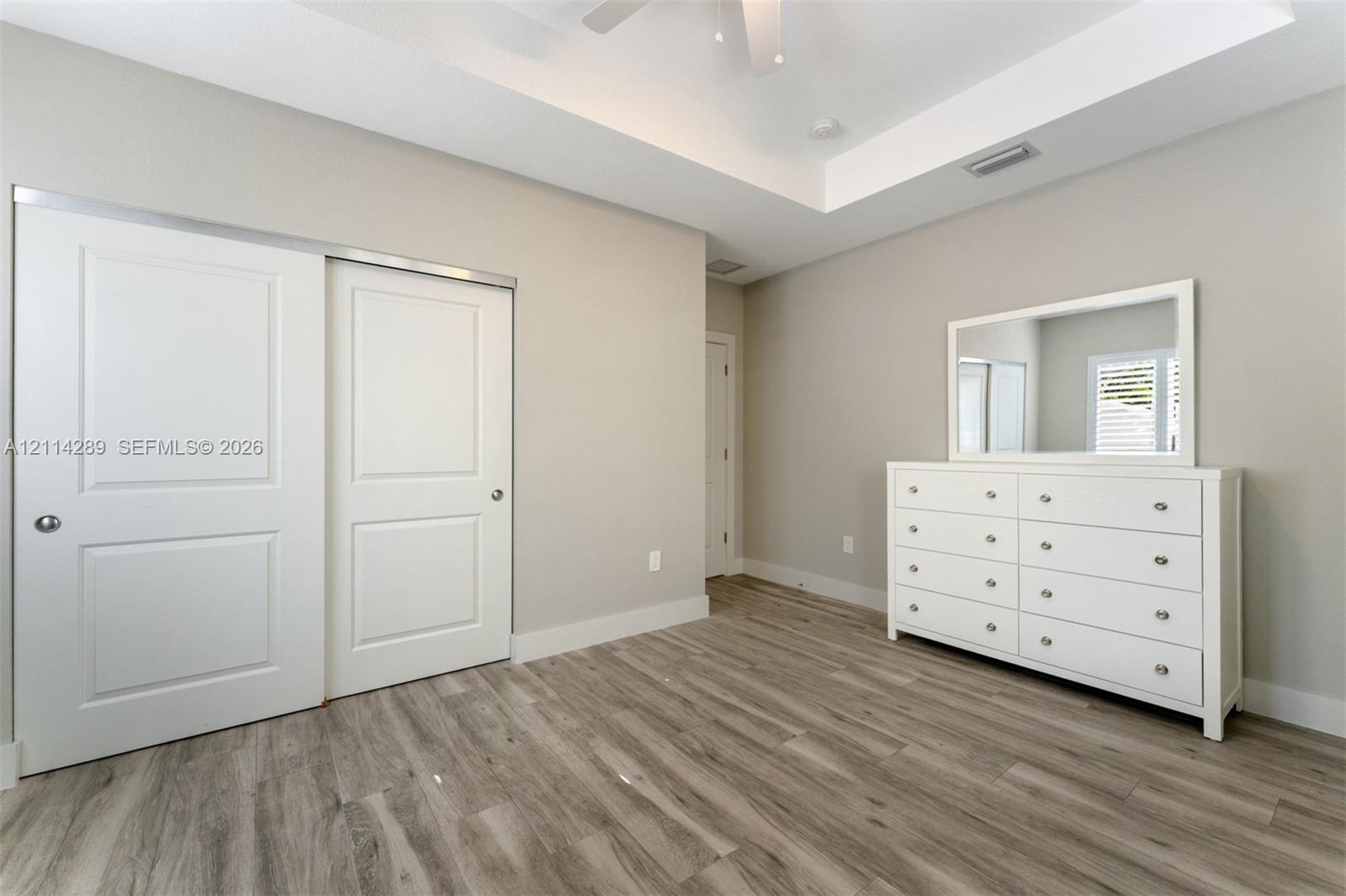 Tray ceiling, wood-finish flooring, sliding panel closet doors, and recessed lighting