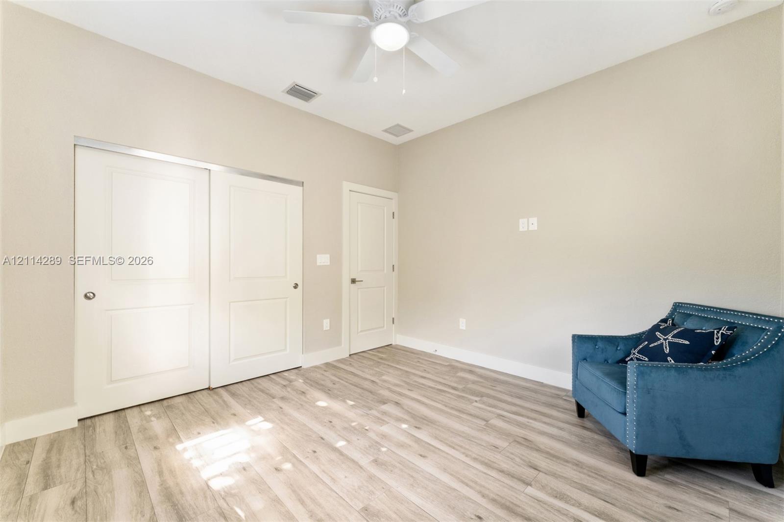 Room featuring wood-finish flooring, high ceilings, ceiling fan with integrated lighting, and dual-panel closet doors