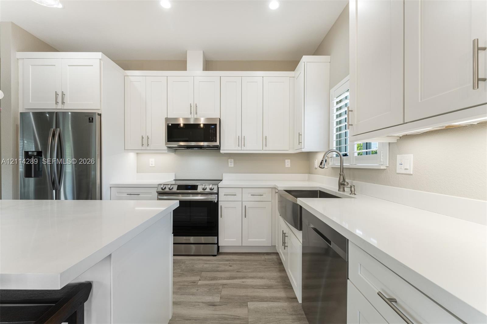 Kitchen featuring white shaker-style cabinetry, quartz countertops, a farmhouse-style stainless steel sink, stainless steel appliances, and wood-finish flooring