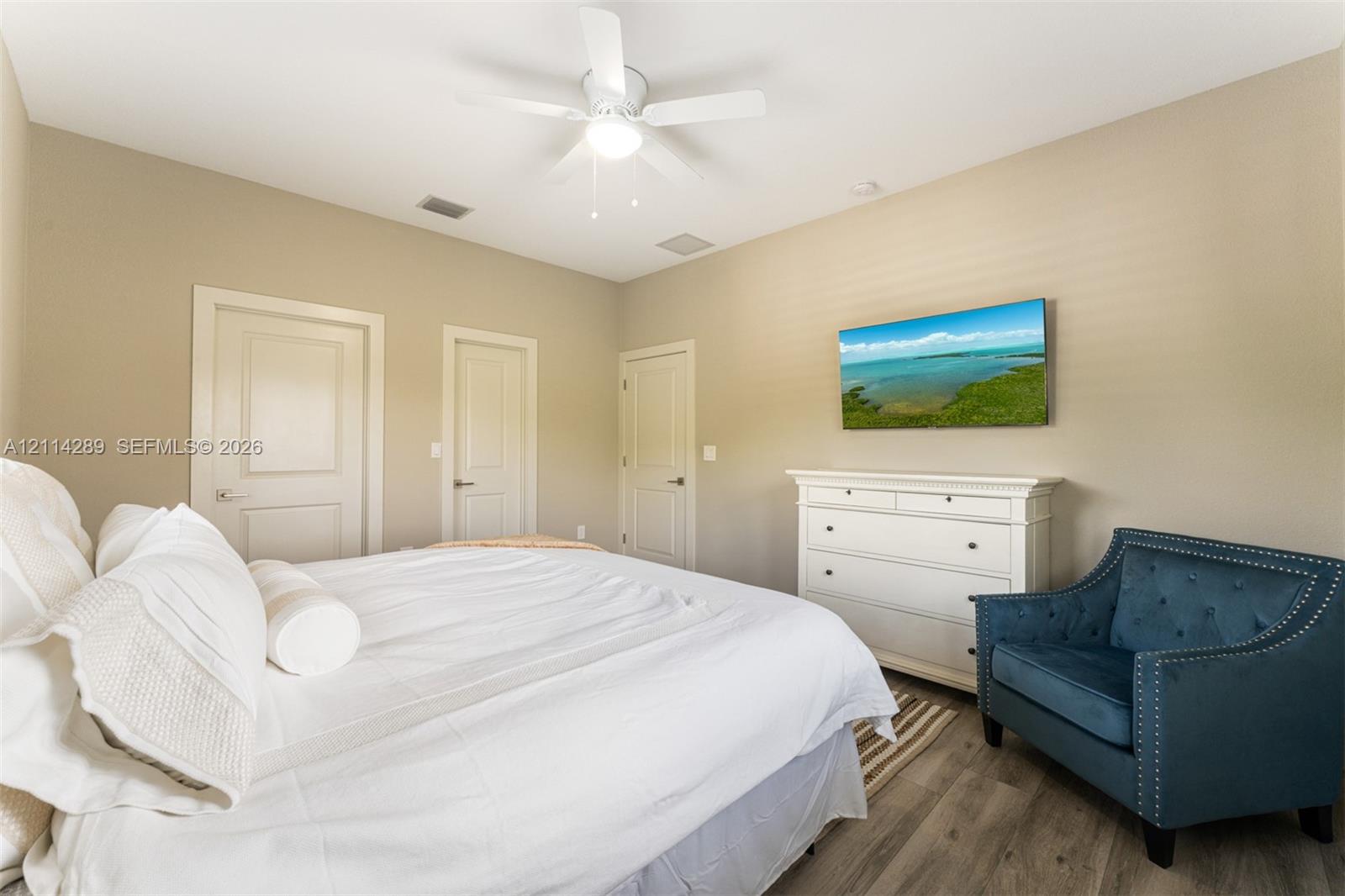 Room featuring wood-finish flooring, a white ceiling fan with integrated lighting, and three interior doors with neutral hardware