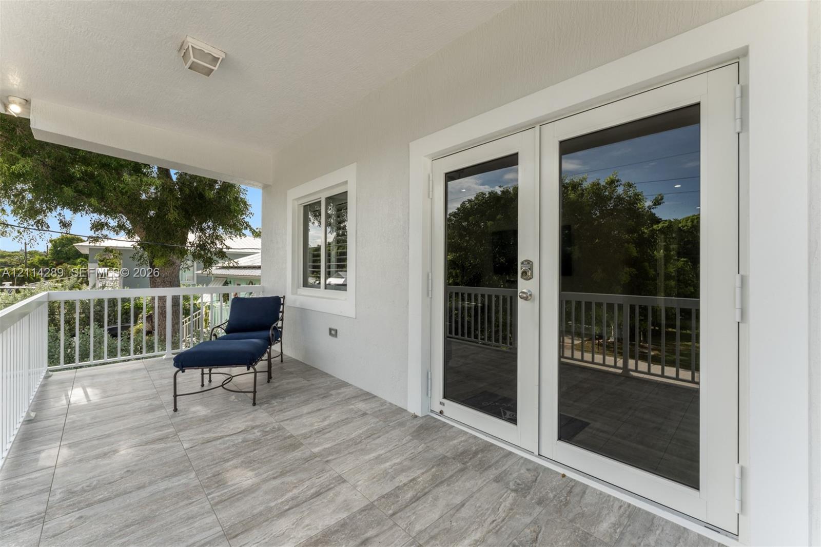 Covered balcony featuring wood-finish tile flooring, white metal railing, and glass-paned double doors