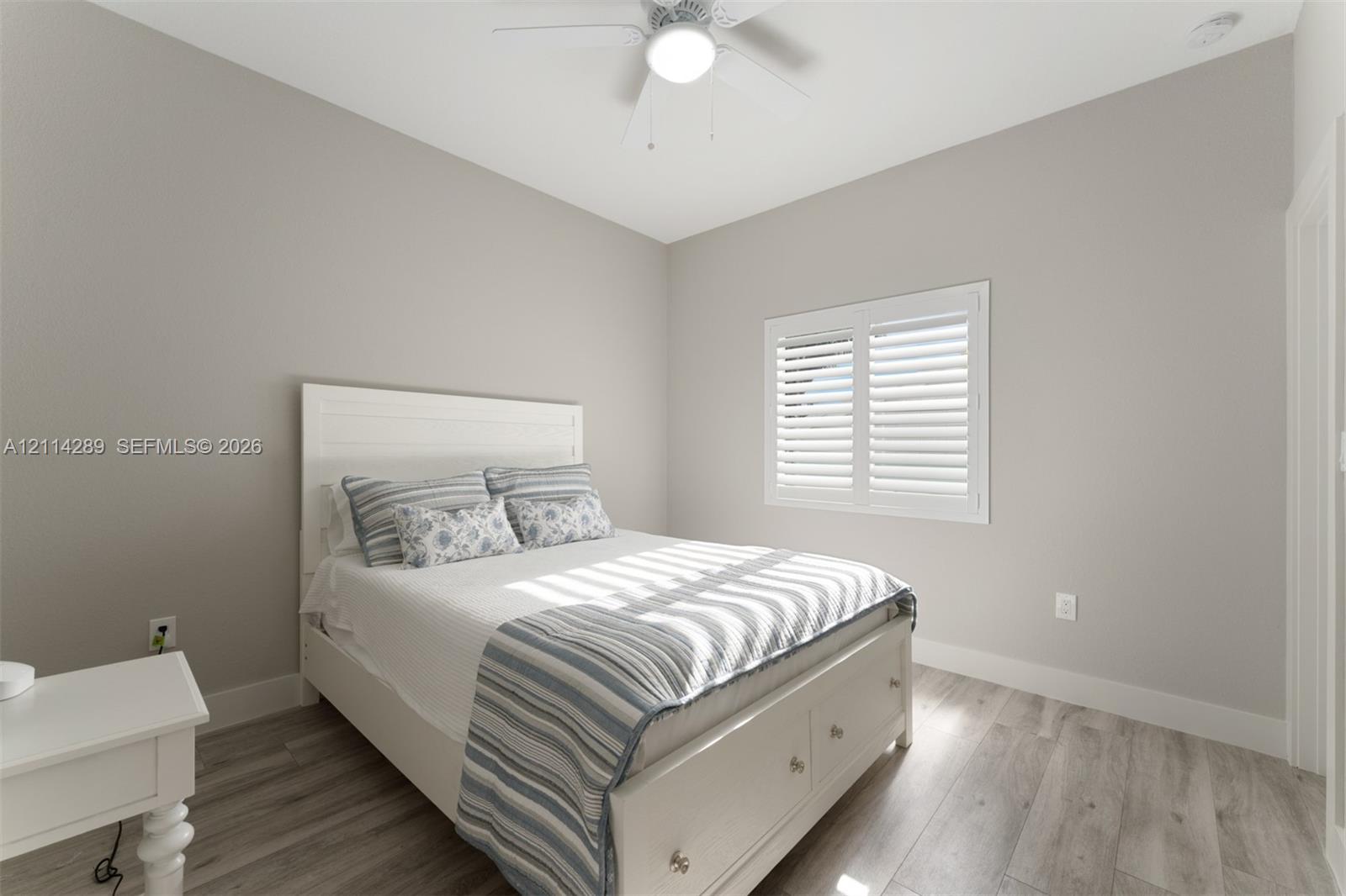 Neutral-toned interior featuring wood-finish flooring, white plantation shutters, and a ceiling fan with integrated lighting