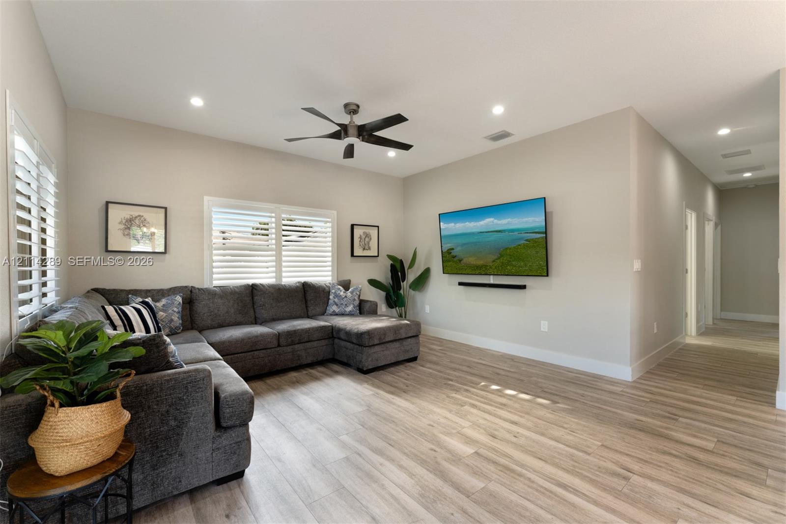 Living area featuring wood-finish flooring, recessed lighting, a ceiling fan, and plantation shutters
