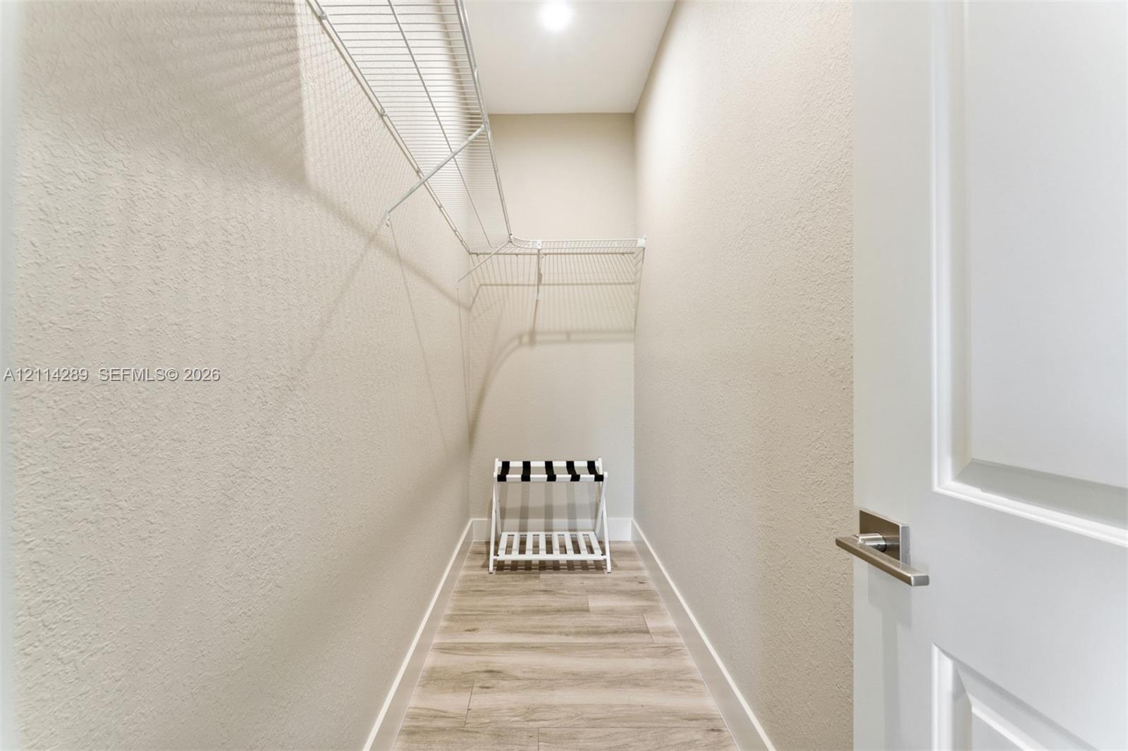 Walk-in closet featuring wood-finish flooring, white paneled door with brushed nickel hardware, and multi-level wire shelving