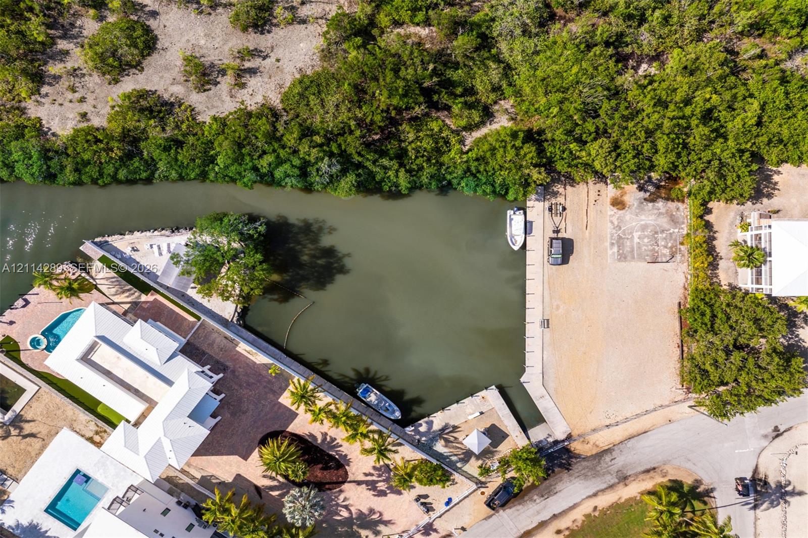 Aerial perspective of a waterfront property featuring a deep-water boat slip, a private canal bulkhead, an in-ground swimming pool, and paved patio surfaces