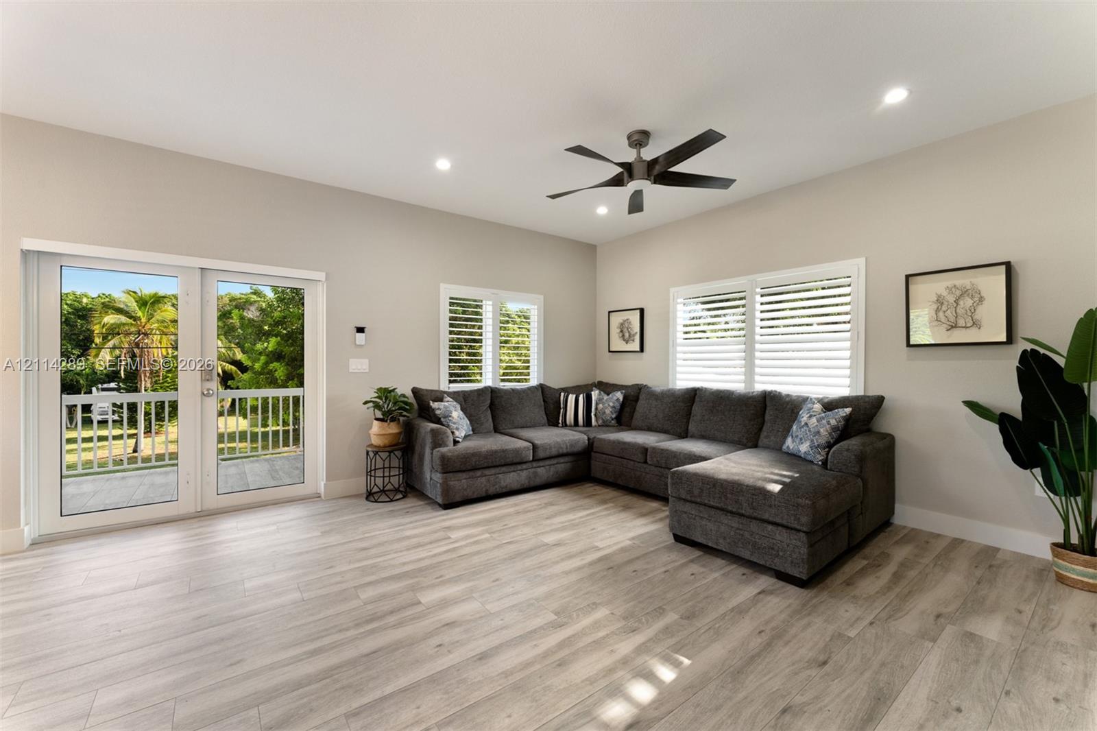 Living area featuring wood-finish flooring, recessed lighting, a modern ceiling fan, shutter-style window coverings, and dual glass-panel doors