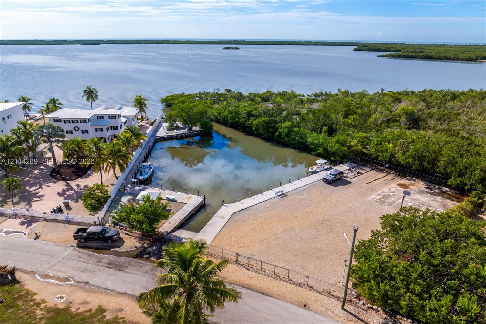 Waterfront property featuring a private concrete boat slip, gravel lot, perimeter fencing, and mature palm trees