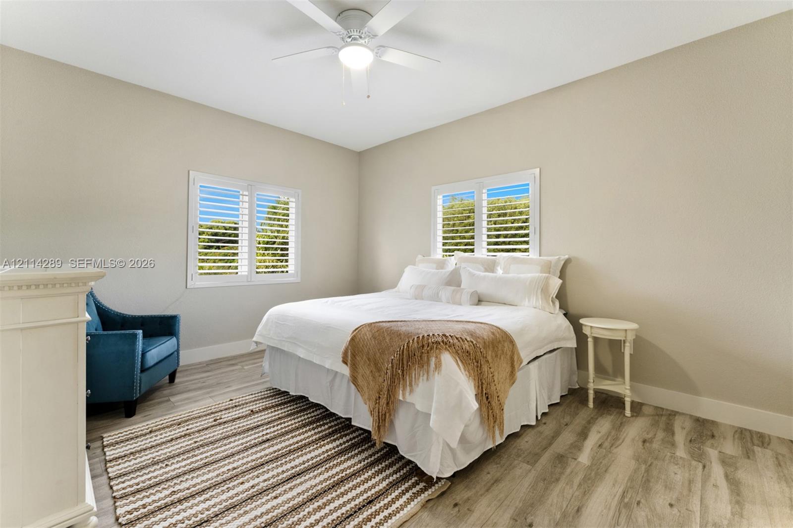 Room featuring wood-finish flooring, white plantation shutters, and a central ceiling fan with integrated lighting