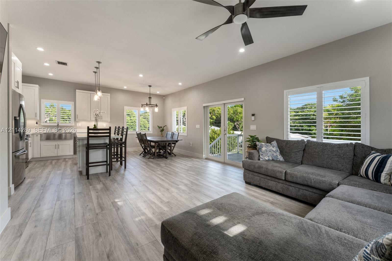 Open-concept living space featuring wood-finish flooring, recessed lighting, white shaker-style cabinetry, stainless steel apron-front sink, and dual glass paneled doors