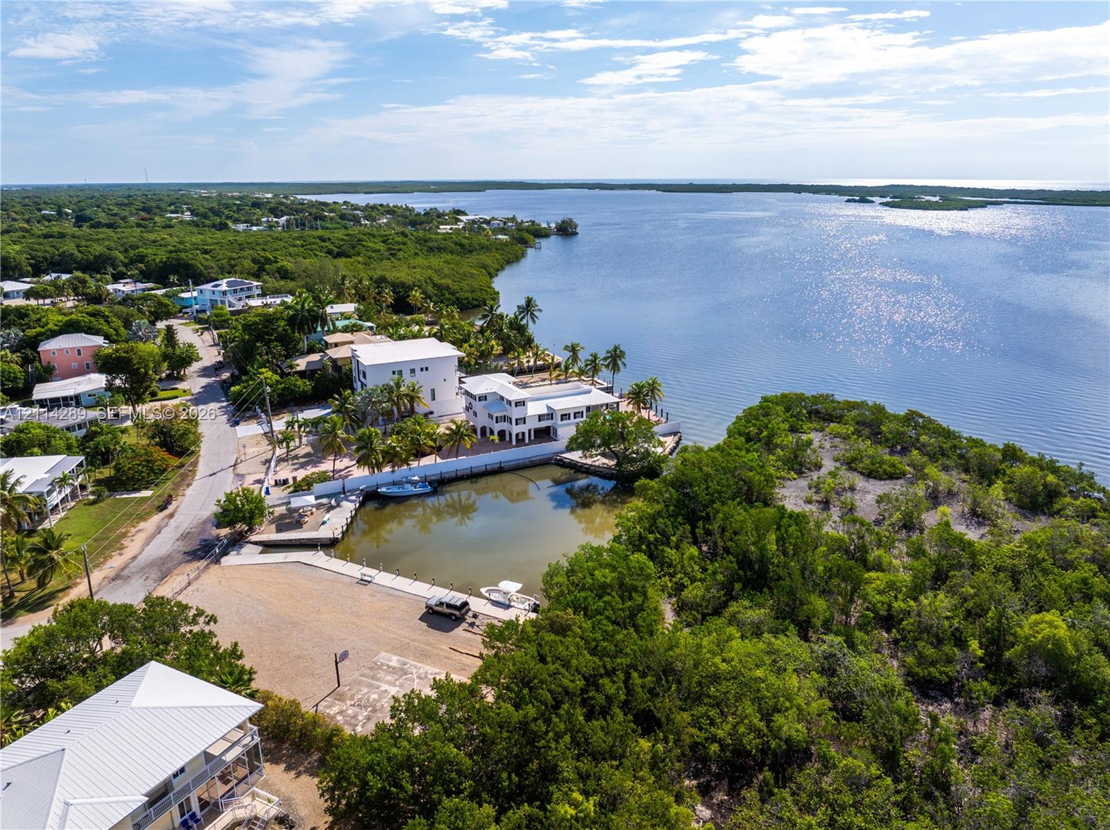Waterfront multi-level residence featuring a private boat slip, dock infrastructure, balcony terraces, and an expansive paved motor court