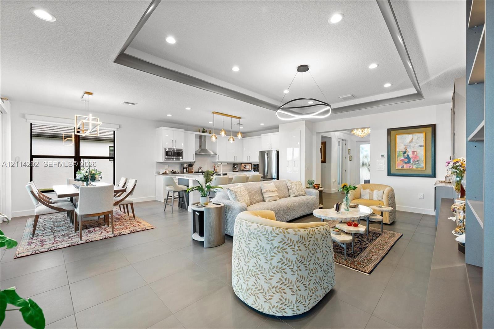 Open concept living space featuring a tray ceiling, recessed lighting, tile flooring, and a kitchen equipped with a large island and stainless steel appliances