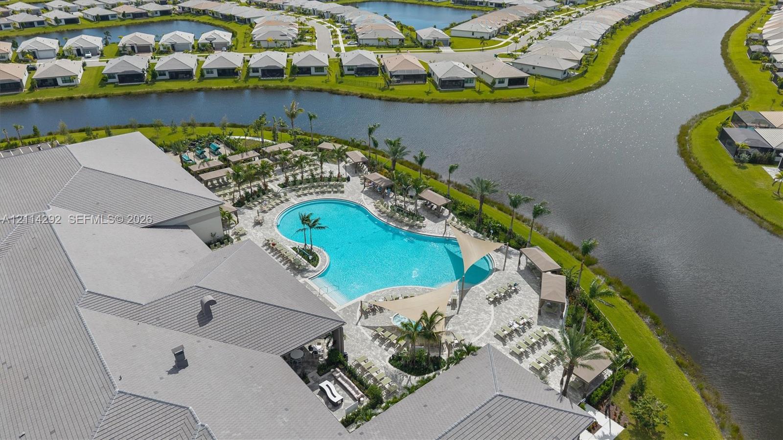 Aerial perspective of a community facility featuring a resort-style swimming pool, paver-stone pool deck, shade structures, and waterfront positioning