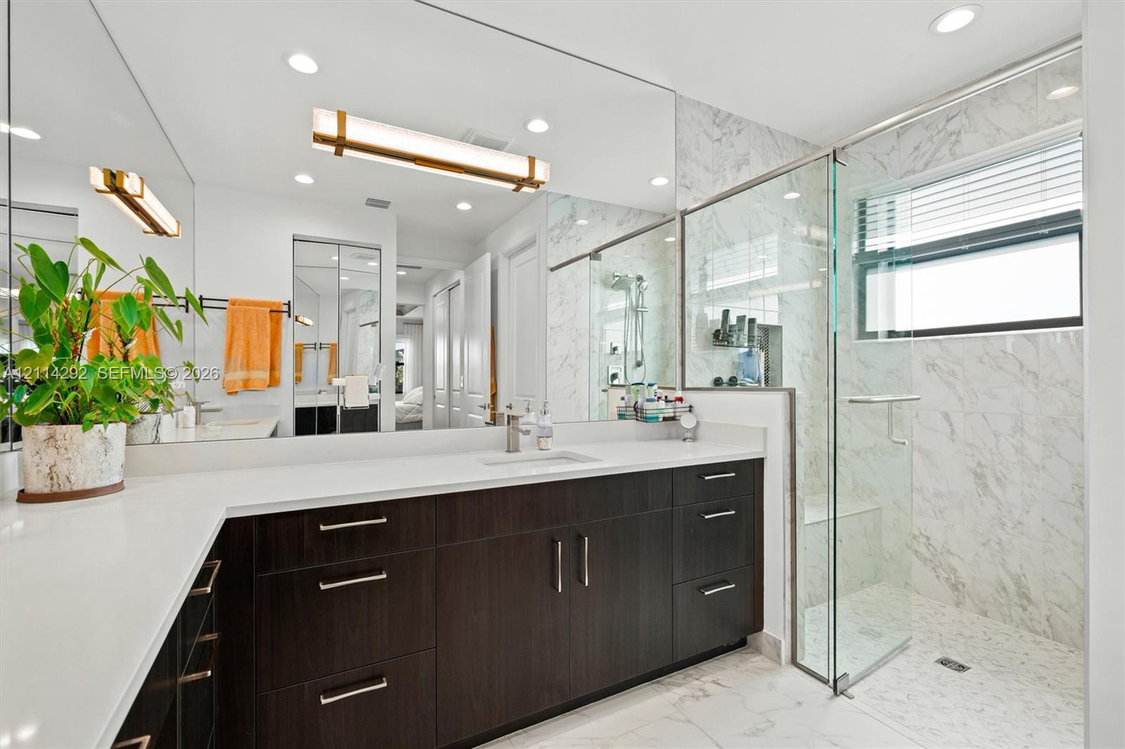 Bathroom featuring a dual-sink dark wood vanity with white countertops, a full-width mirror, recessed lighting, and a glass-enclosed shower with stone-tile surround