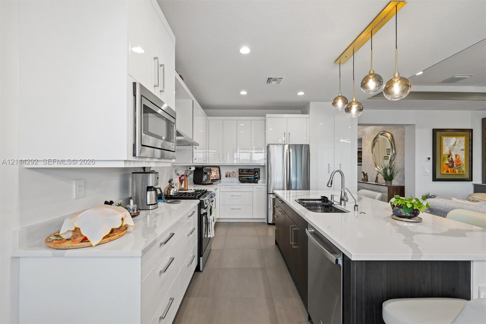 Kitchen featuring high-gloss white cabinetry, expansive stone countertops, stainless steel appliances, a central island, and modern pendant lighting
