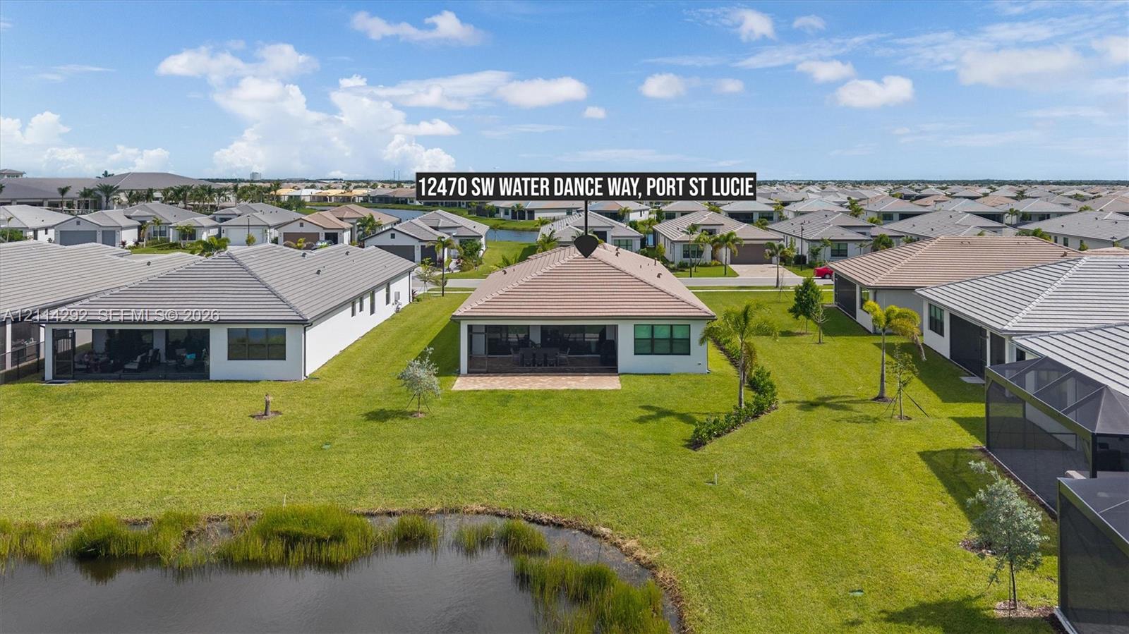 Aerial perspective of a residential property featuring a tiled roof, screened rear patio, and expansive lawn area backing to a waterfront pond