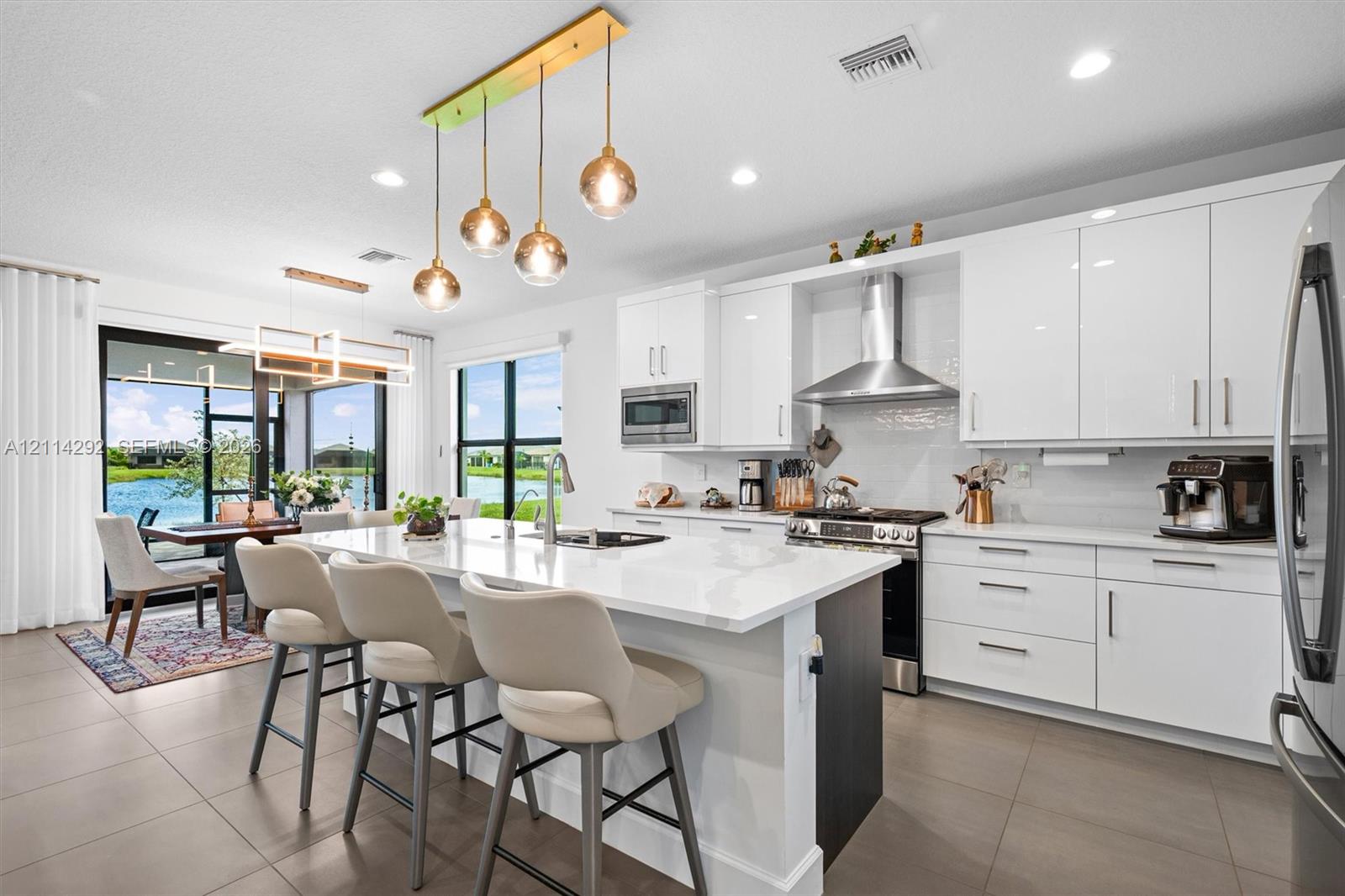 Kitchen featuring high-gloss white cabinetry, a large central island with white quartz countertops, stainless steel appliances, and multi-pendant lighting