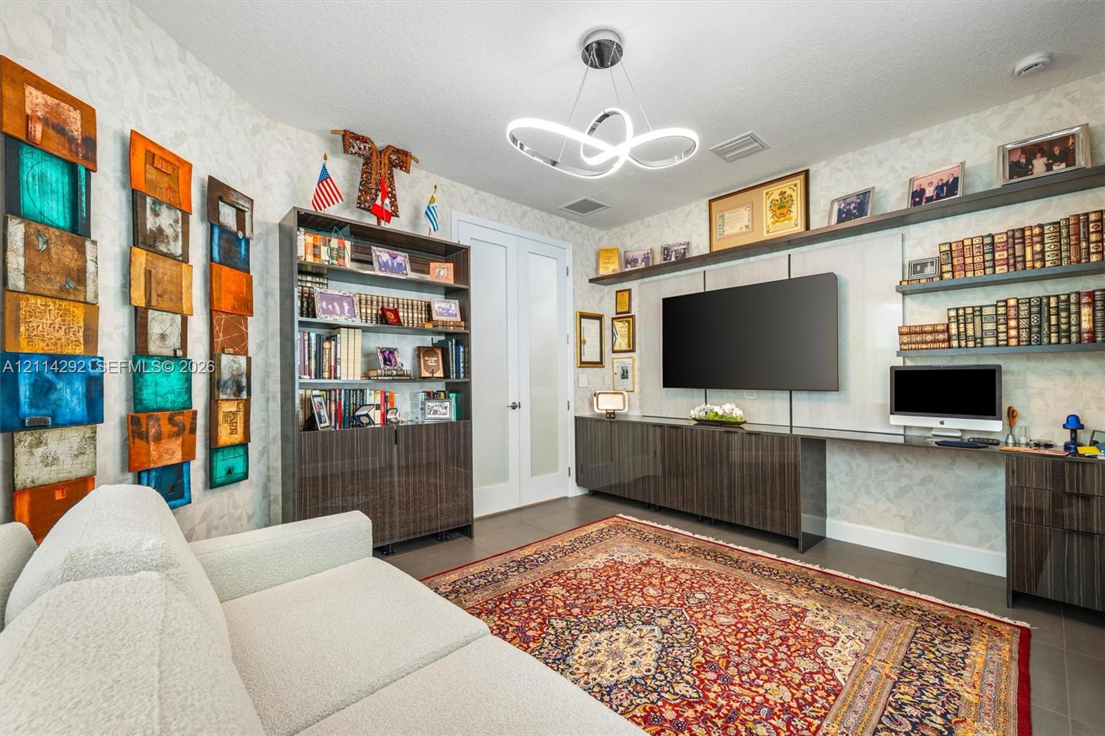 Custom built-in cabinetry with integrated workspace, floating wall shelving, modern minimalist ceiling fixture, and double glass-panel doors