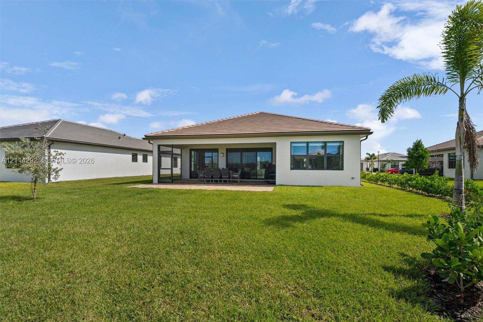 Exterior rear elevation featuring a stucco facade, hipped roofline, covered screened-in patio, and expansive lawn with mature palm landscaping
