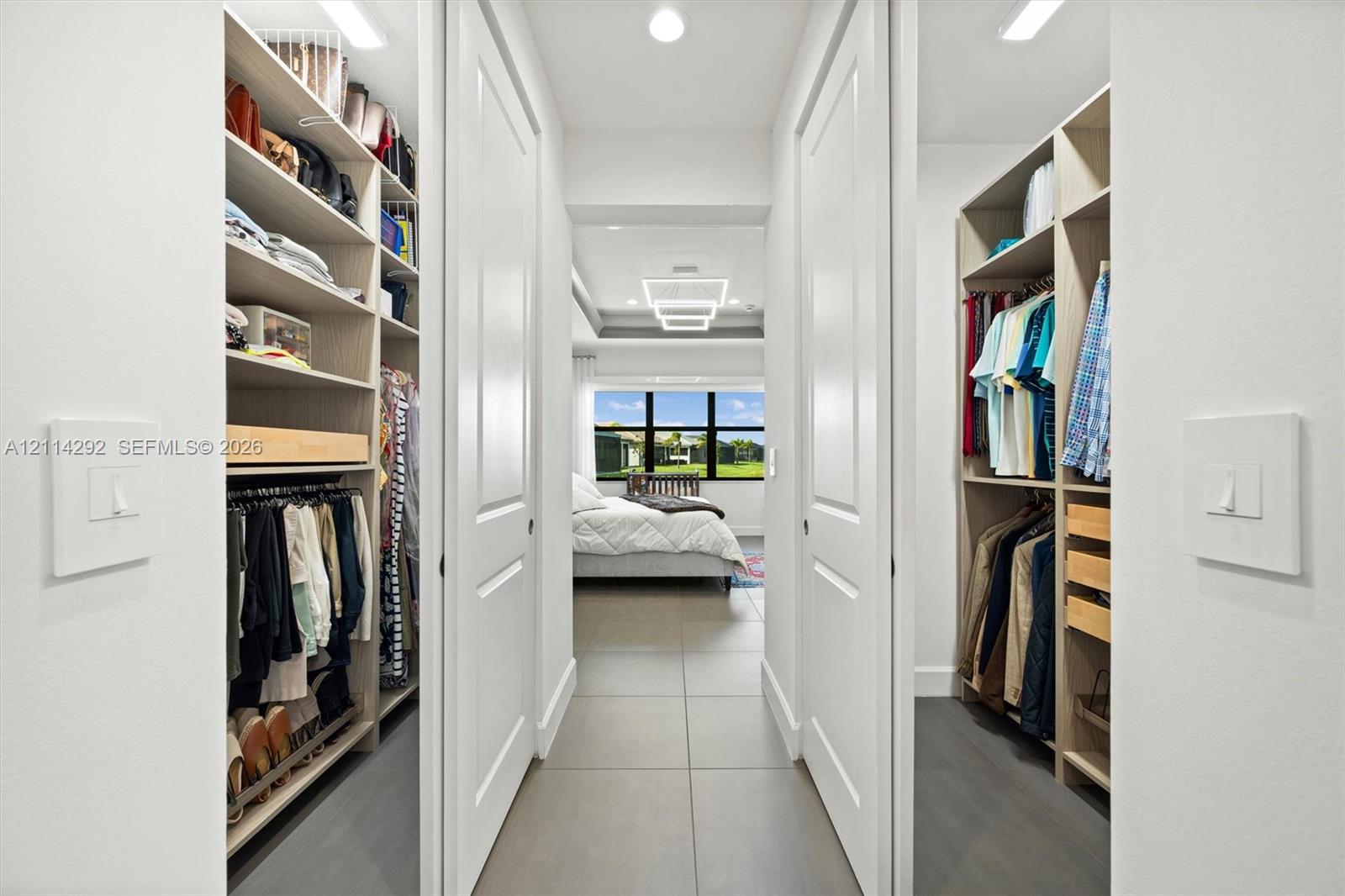Walk-in closet featuring floor-to-ceiling built-in shelving, hanging rods, pull-out storage drawers, and large-format tile flooring