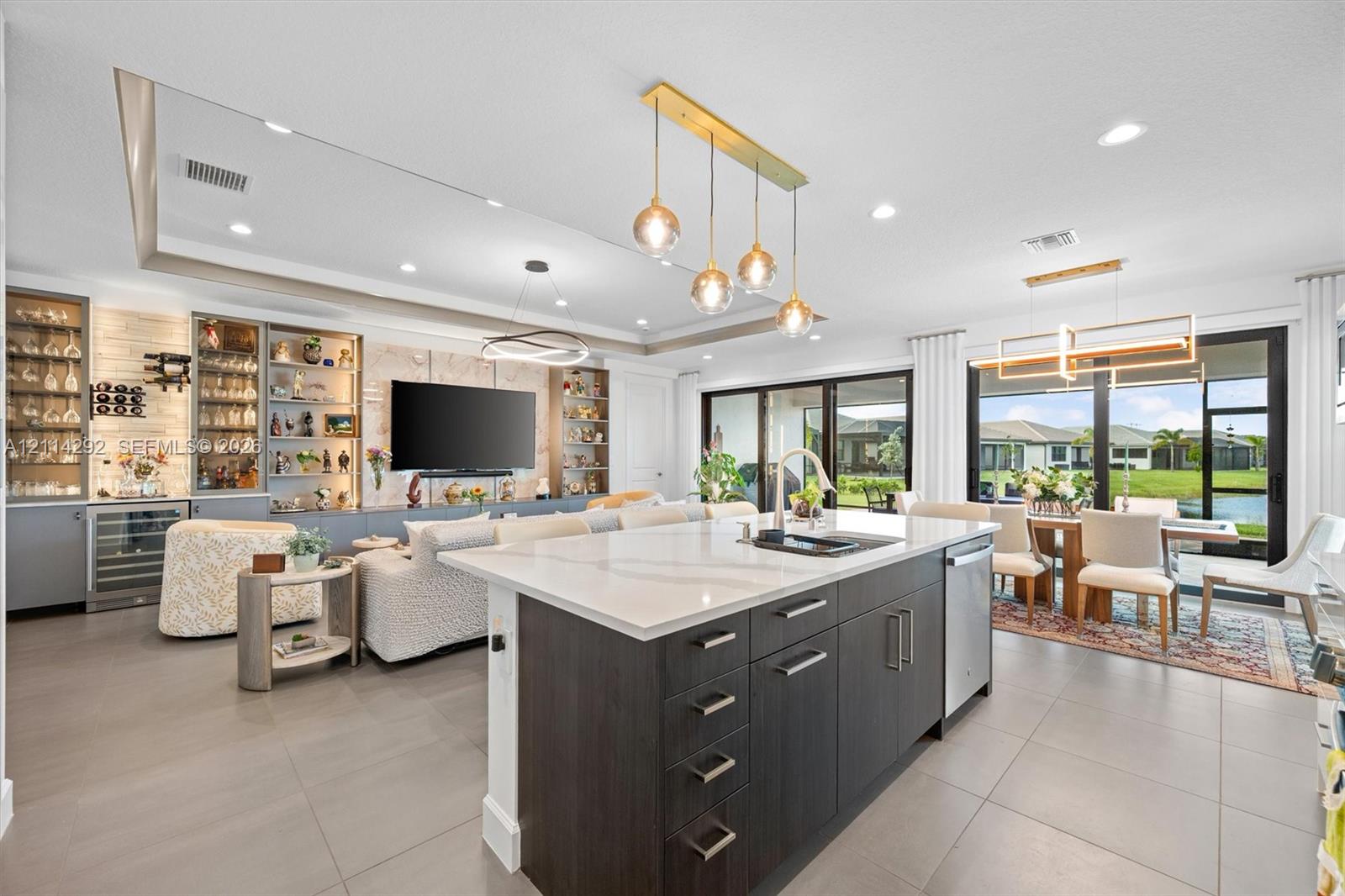 Center island with quartz countertop and undermount sink, dark-toned cabinetry, built-in display shelving with integrated lighting, oversized sliding glass doors, and recessed ceiling lighting