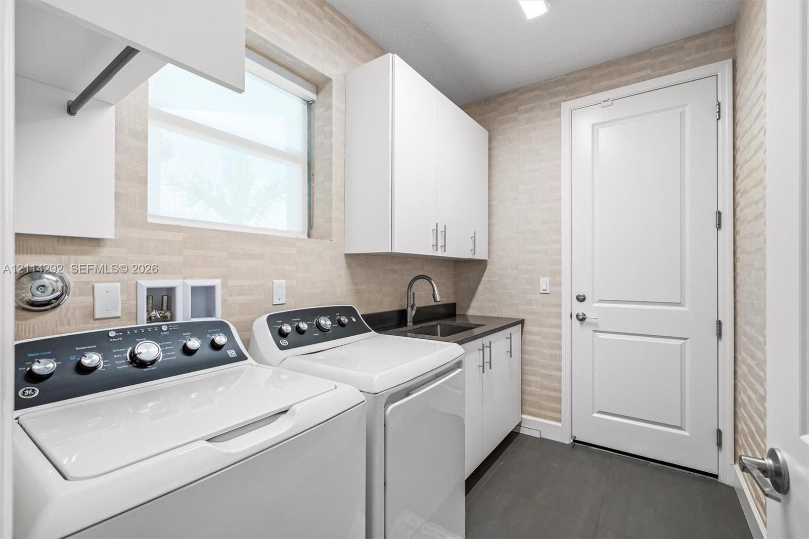 Utility room featuring textured wall tile, white shaker-style cabinetry, a dark countertop with a built-in sink, and slate-finish flooring