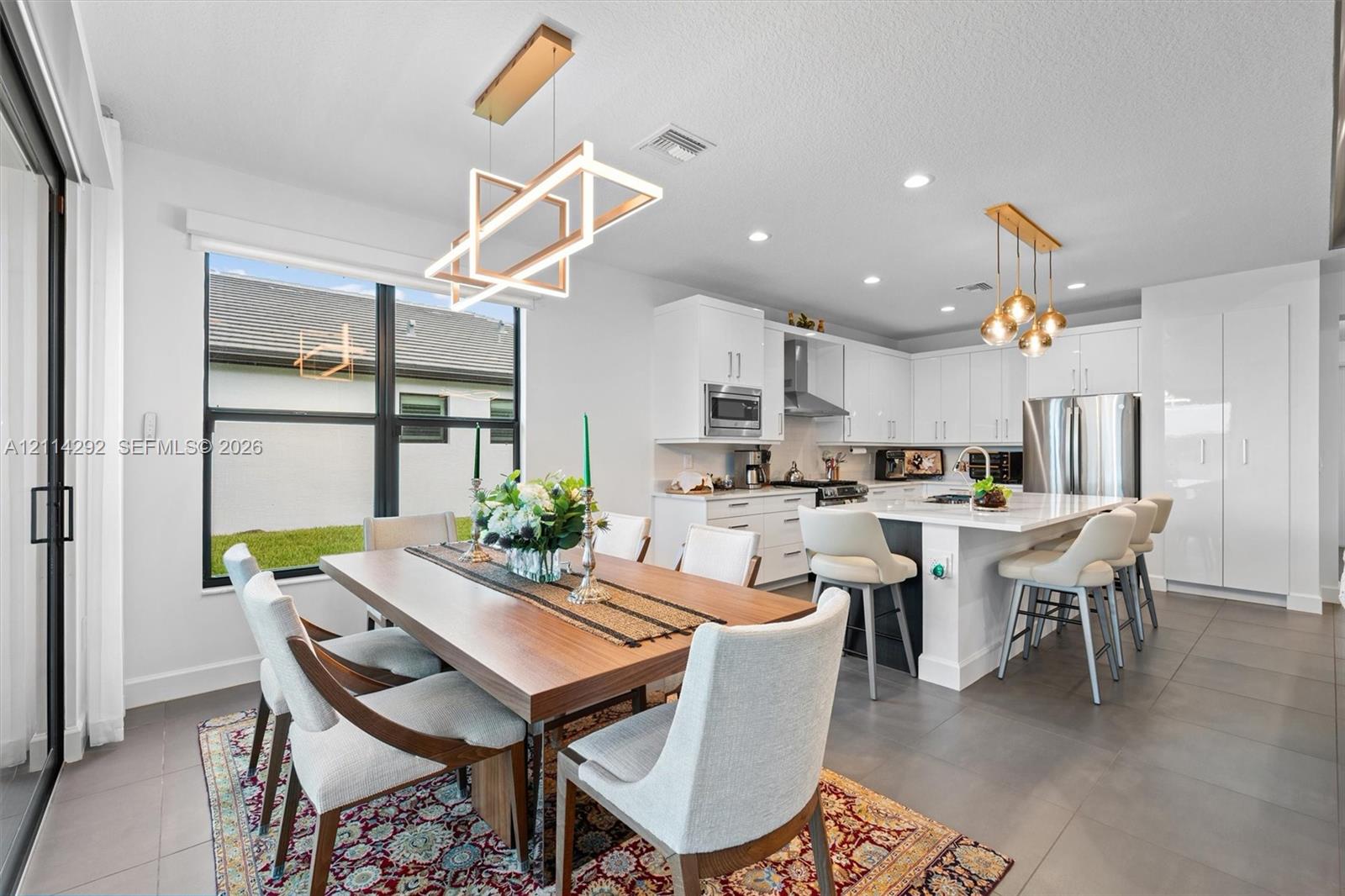 Kitchen featuring white cabinetry, an expansive central island with stone-surface countertop, stainless steel appliances, large-format tile flooring, and geometric modern lighting fixtures