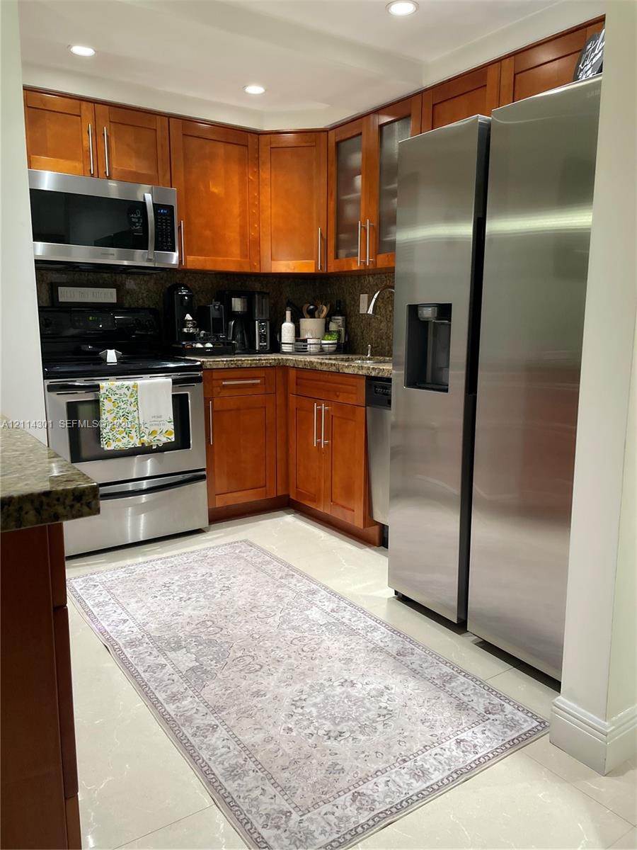 Kitchen featuring wood-finish cabinetry, stone-surface countertops, stainless steel appliances, glass-front upper cabinet doors, and recessed lighting