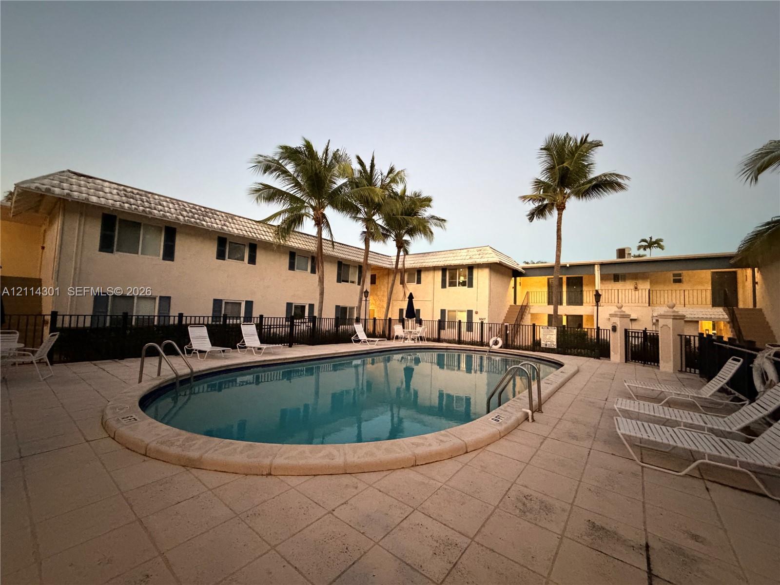 Oval swimming pool featuring a concrete deck, metal perimeter fencing, and mature palm trees
