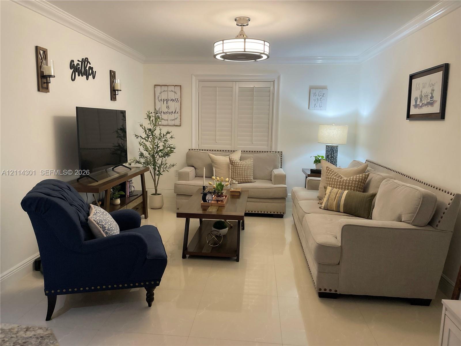 Living area featuring large-format tile flooring, crown molding, plantation shutters, and a modern drum-style ceiling light fixture