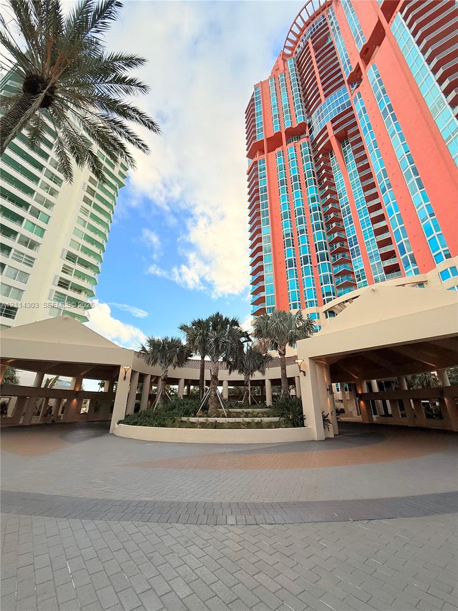 Multi-story high-rise building with a glass facade, circular paver driveway, covered porte-cochre, and a central landscaped courtyard featuring mature palms