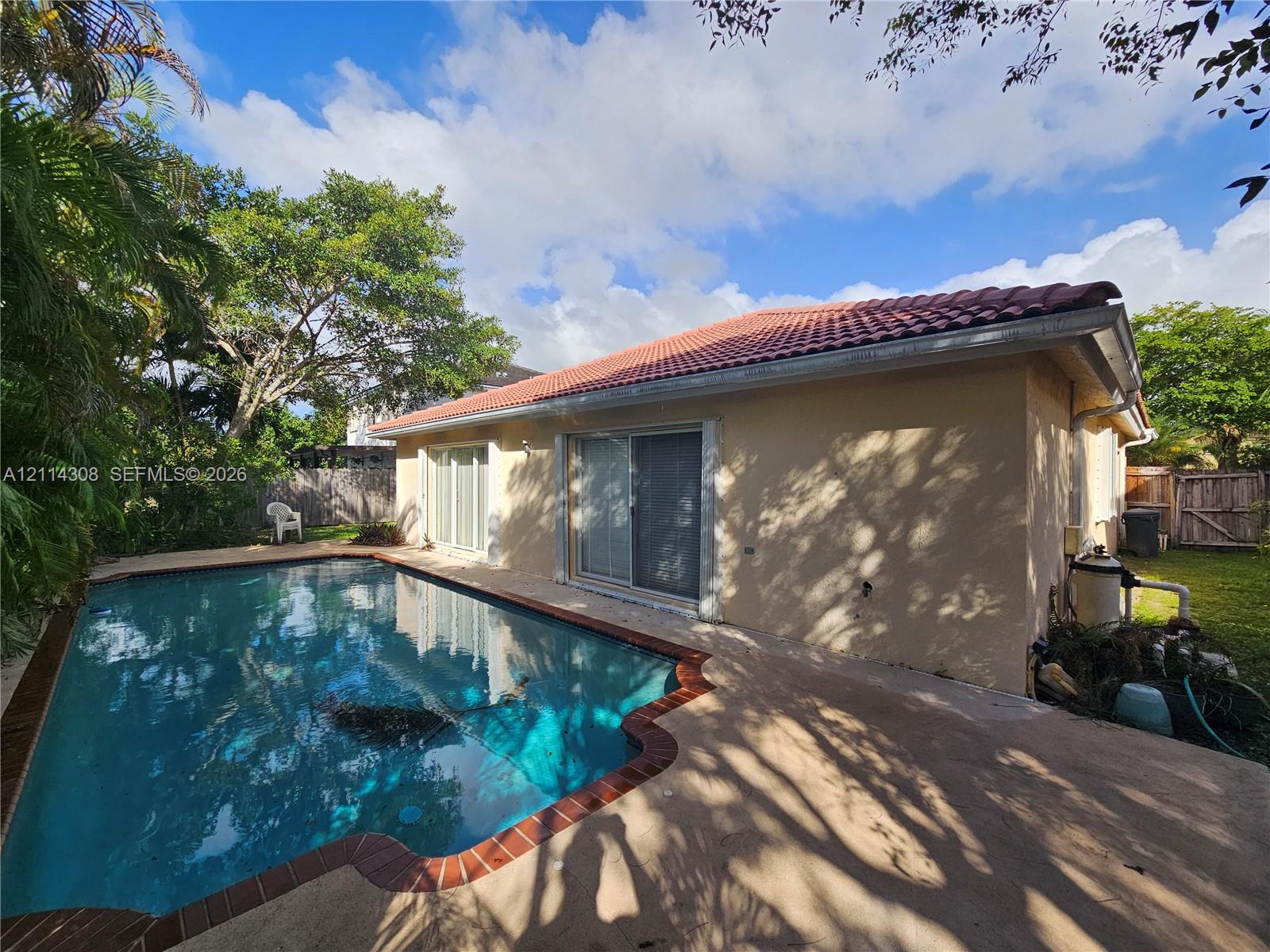 Inground swimming pool with a brick-trimmed border, concrete patio, stucco exterior, and a tiled hip roof