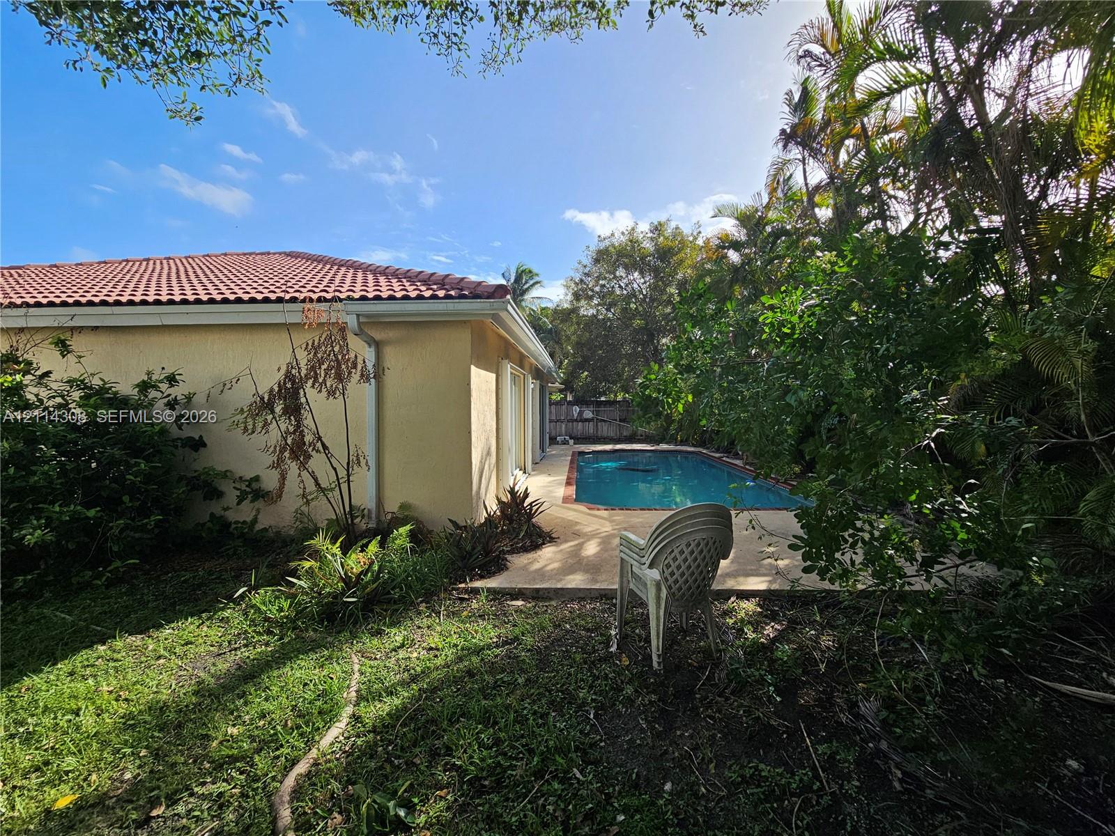 Backyard featuring an in-ground swimming pool, concrete patio, tile roof, and mature landscaping