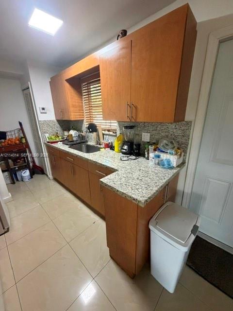 Kitchen featuring light-finish wood cabinetry, stone-texture countertops, tile flooring, and a stainless steel undermount sink Kitchen featuring light-finish wood cabinetry, stone-texture countertops, tile flooring, and a stainless steel undermount sink