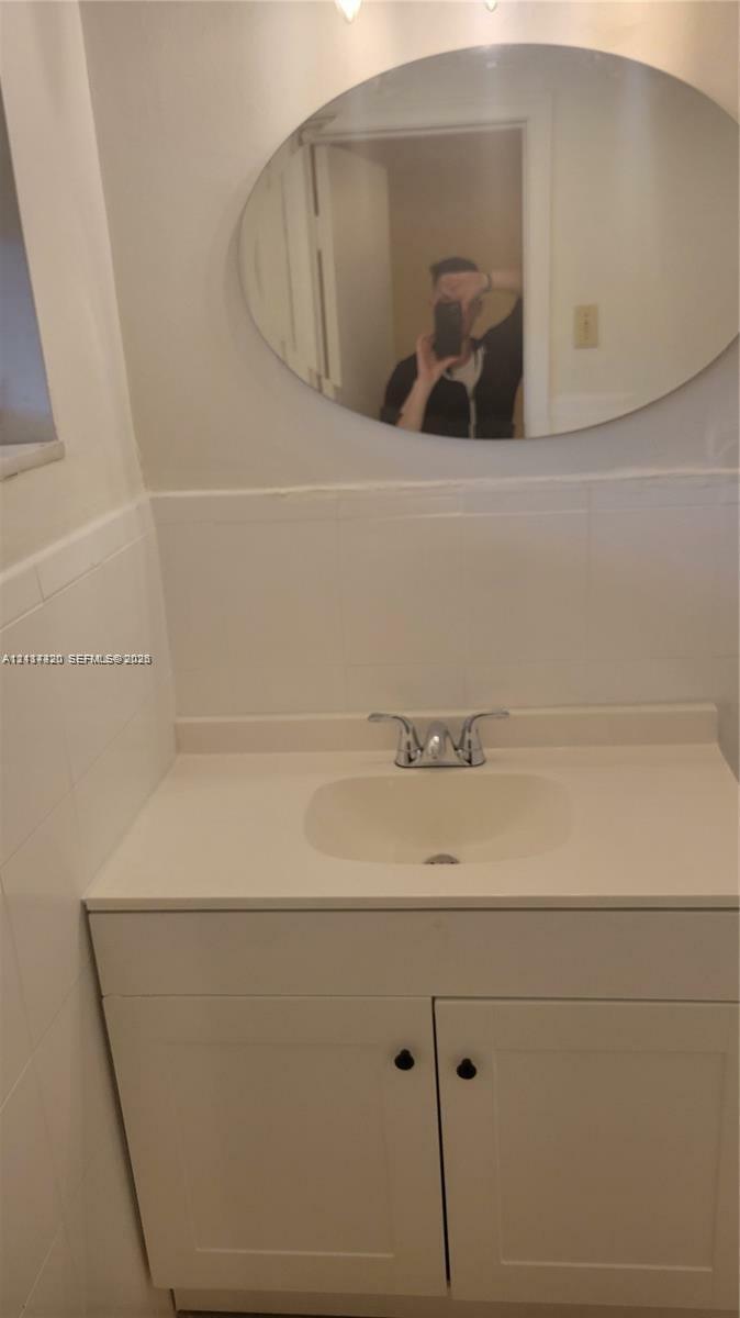 Bathroom vanity featuring a solid-surface countertop, an integrated sink basin, chrome dual-handle faucet, oval mirror, and tiled wall surround