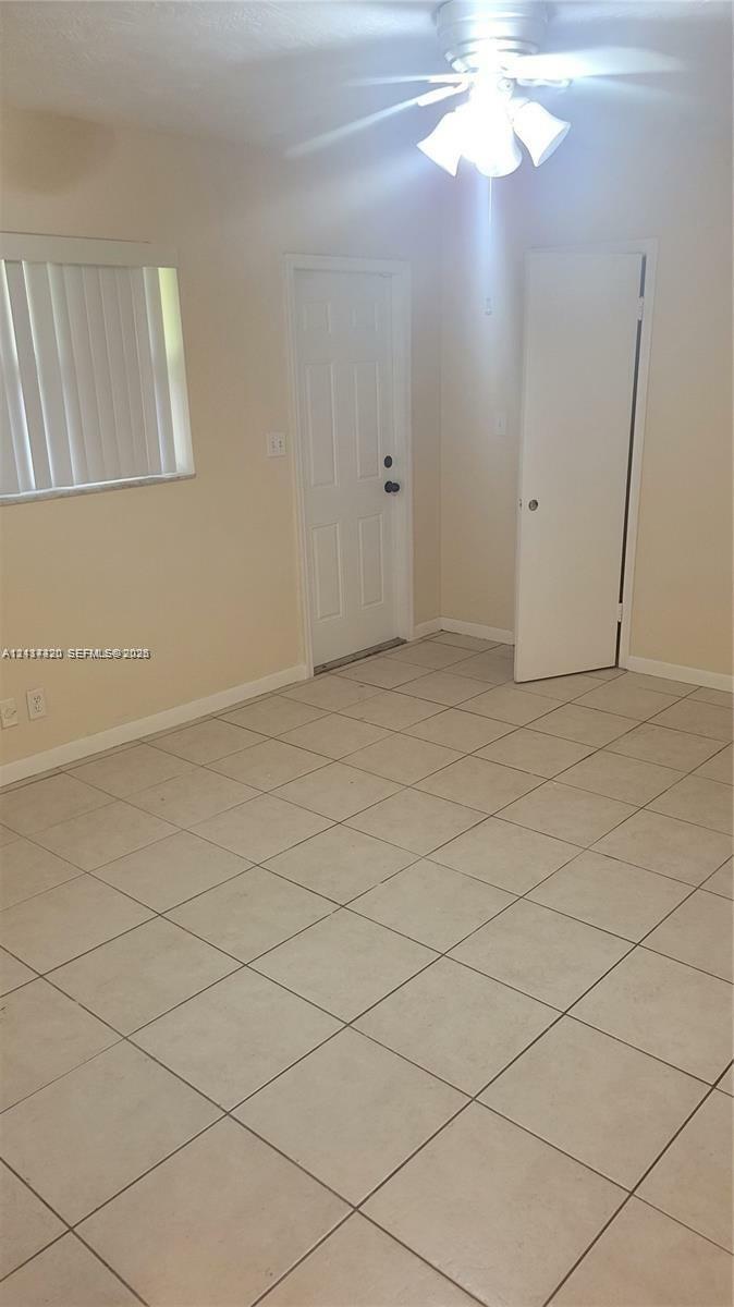 Neutral-toned interior space featuring large-format ceramic floor tiles, a ceiling-mounted light fixture with multi-directional shades, a six-panel exterior door, and a single-panel interior door