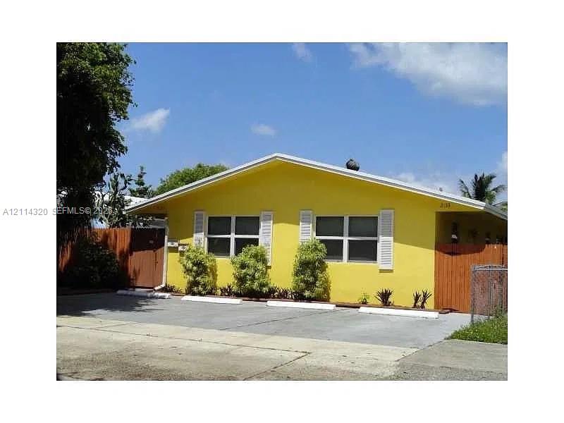 Single-story exterior featuring a vibrant stucco finish, multi-pane windows with louvered shutters, gabled roofline, and an asphalt parking area with concrete wheel stops