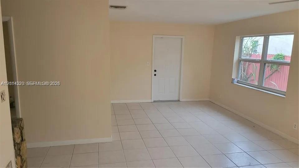 Neutral-toned interior featuring ceramic tile flooring, a large multi-pane window, and a solid-panel exterior door Neutral-toned interior featuring ceramic tile flooring, a large multi-pane window, and a solid-panel exterior door