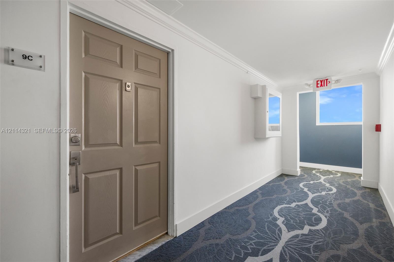 Six-panel entryway door with brushed metal hardware, decorative patterned carpeting, and crown molding