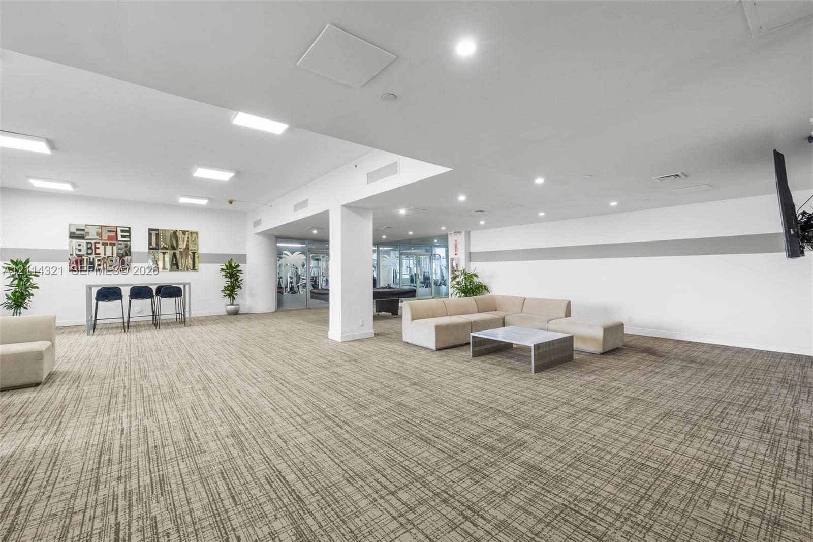 Open-concept recreation area featuring neutral patterned carpeting, recessed ceiling lighting, a structural support column, and floor-to-ceiling glass paneling