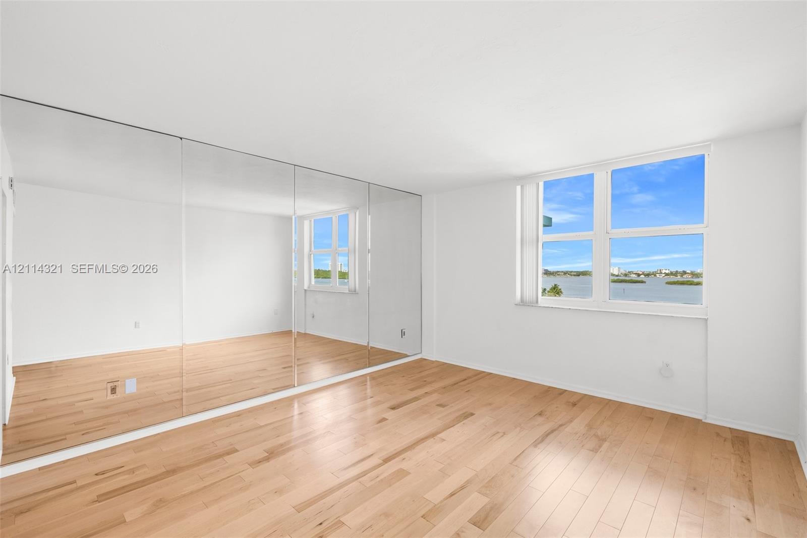 Bright room featuring wood-finish flooring, a floor-to-ceiling mirrored wall, and large windows with water scenery