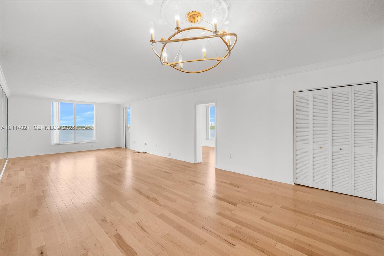 Open-concept interior featuring wood-finish flooring, gold-tone chandelier with decorative ceiling medallion, floor-to-ceiling windows, and bifold closet doors