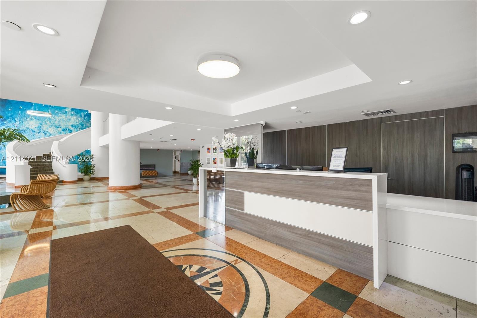 Lobby area featuring a custom reception desk with composite surfacing, recessed lighting, multi-toned stone flooring with inlaid compass motif, and a spiral staircase