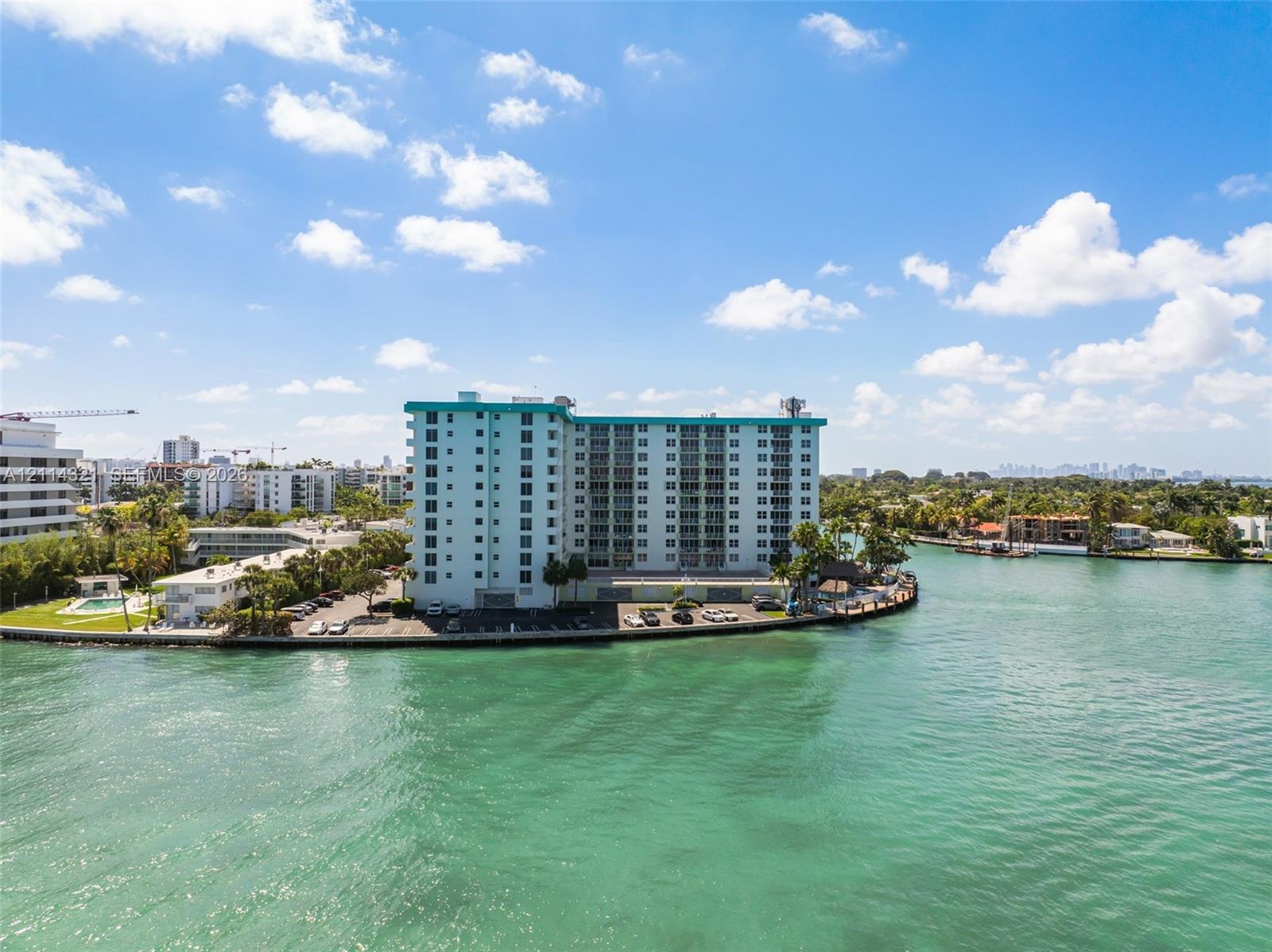 High-rise residential structure situated on a waterfront peninsula, featuring a paved parking lot and established coastal landscaping