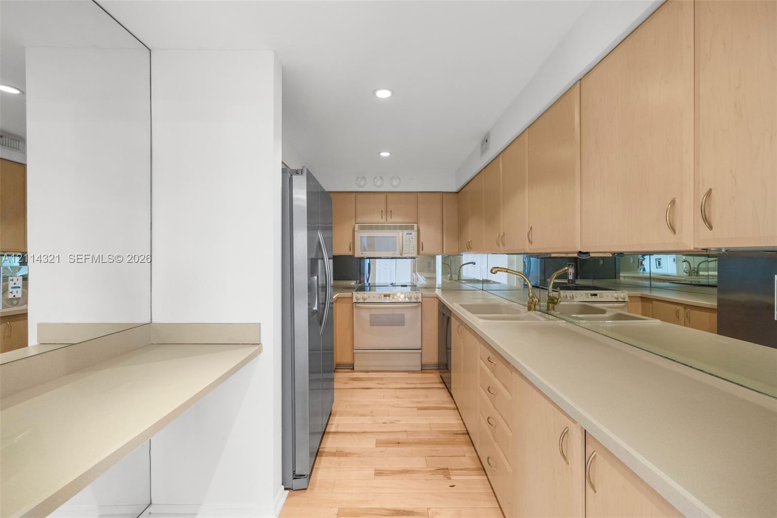 Kitchen featuring flat-panel wood cabinetry, solid-surface countertops, wood-finish flooring, full-height mirror backsplash, and stainless steel refrigerator
