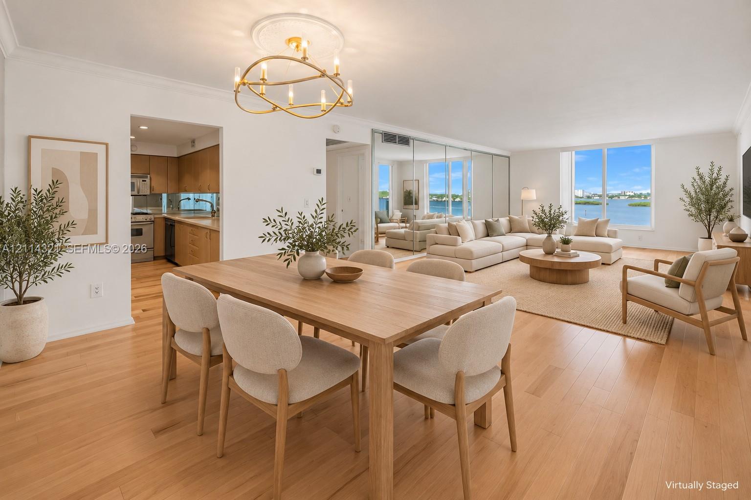 Open-concept living space featuring wood-finish flooring, a modern gold-tone circular chandelier, expansive windows, and a mirrored wall panel