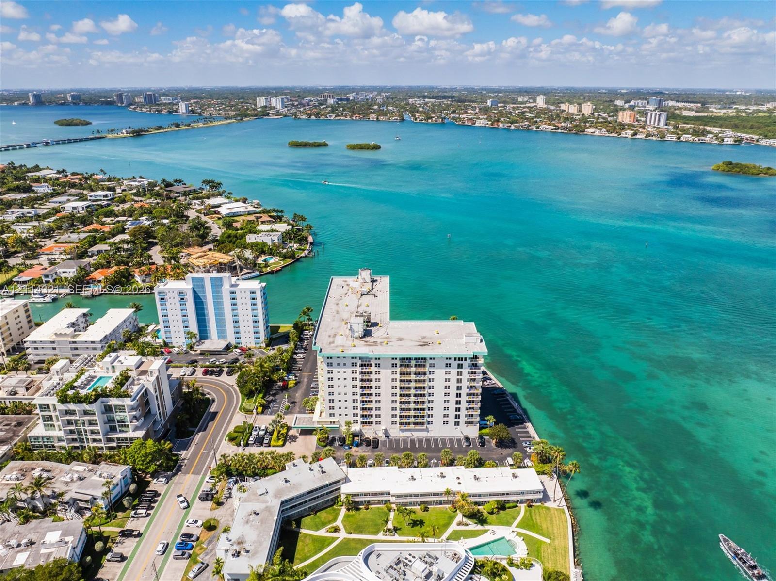 Aerial perspective of waterfront high-rise property featuring shoreline access, surface parking, and exterior balcony structures
