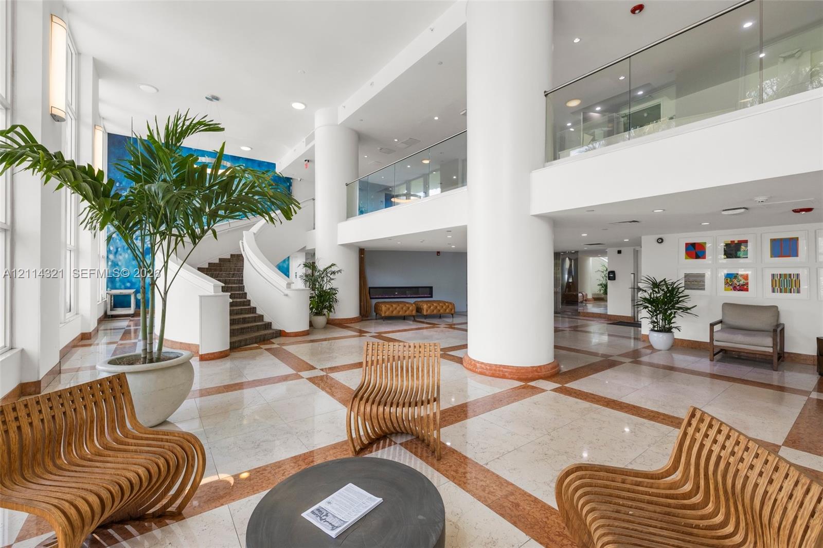 Grand lobby featuring a double-height ceiling, polished tile flooring with inlaid stone detailing, a sweeping staircase with a curved railing, and a glass-paneled mezzanine