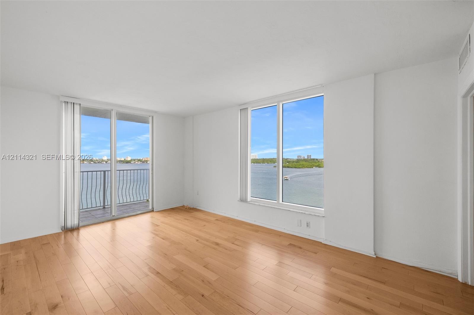 Living area featuring wood-finish flooring, floor-to-ceiling windows, and access to a balcony overlooking a water body